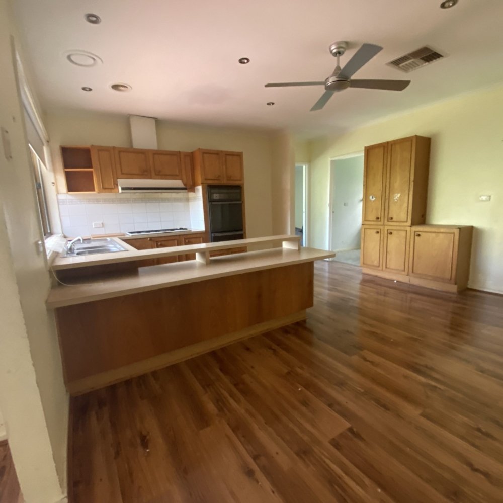 The kitchen before renovation has old cabinets, outdated appliances, and worn countertops.